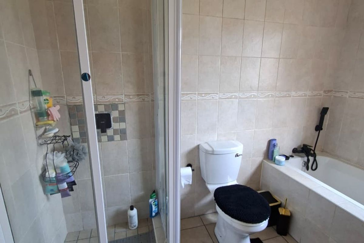 A functional bathroom featuring a separate shower enclosure, bathtub, toilet, and neutral wall and floor tiling.