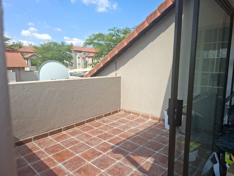 A private balcony featuring terracotta tiled flooring, a sliding glass door entrance, and a parapet wall with views of the surrounding complex.