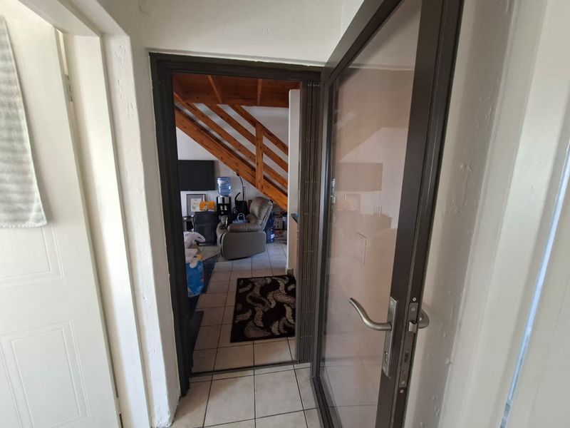 A view through a glass-panelled doorway into a living area featuring tiled flooring and a timber staircase.