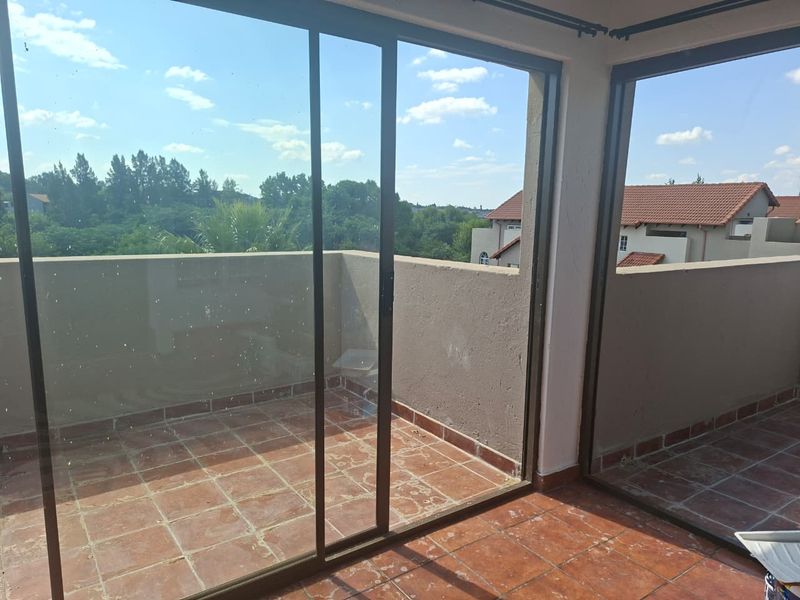 An open-air balcony featuring terracotta tiled flooring, concrete balustrades, and large sliding glass doors providing access to the interior.
