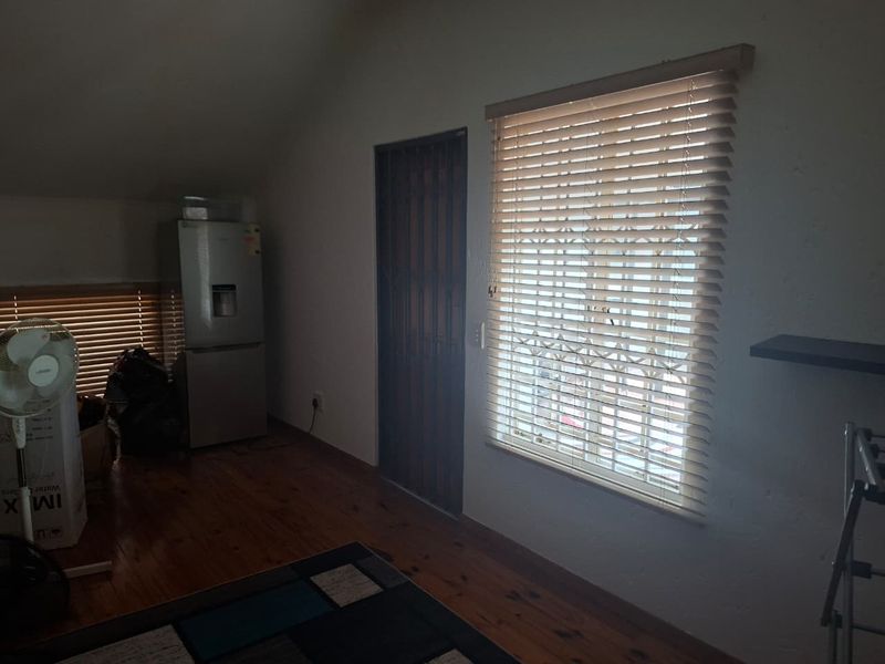 A living area featuring timber flooring, security gate access, and windows fitted with venetian blinds and security bars.