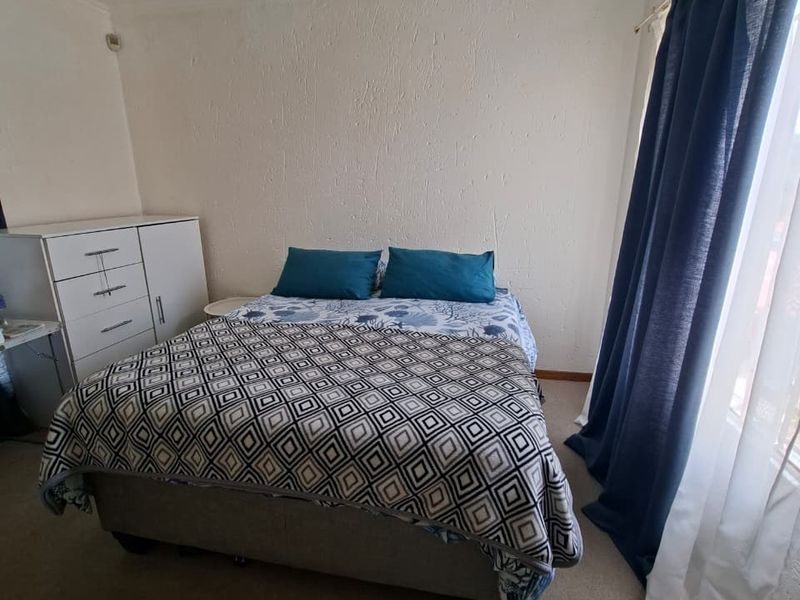 A functional bedroom featuring carpeted flooring, neutral wall finishes, and natural light provided by a window with curtain tracks.