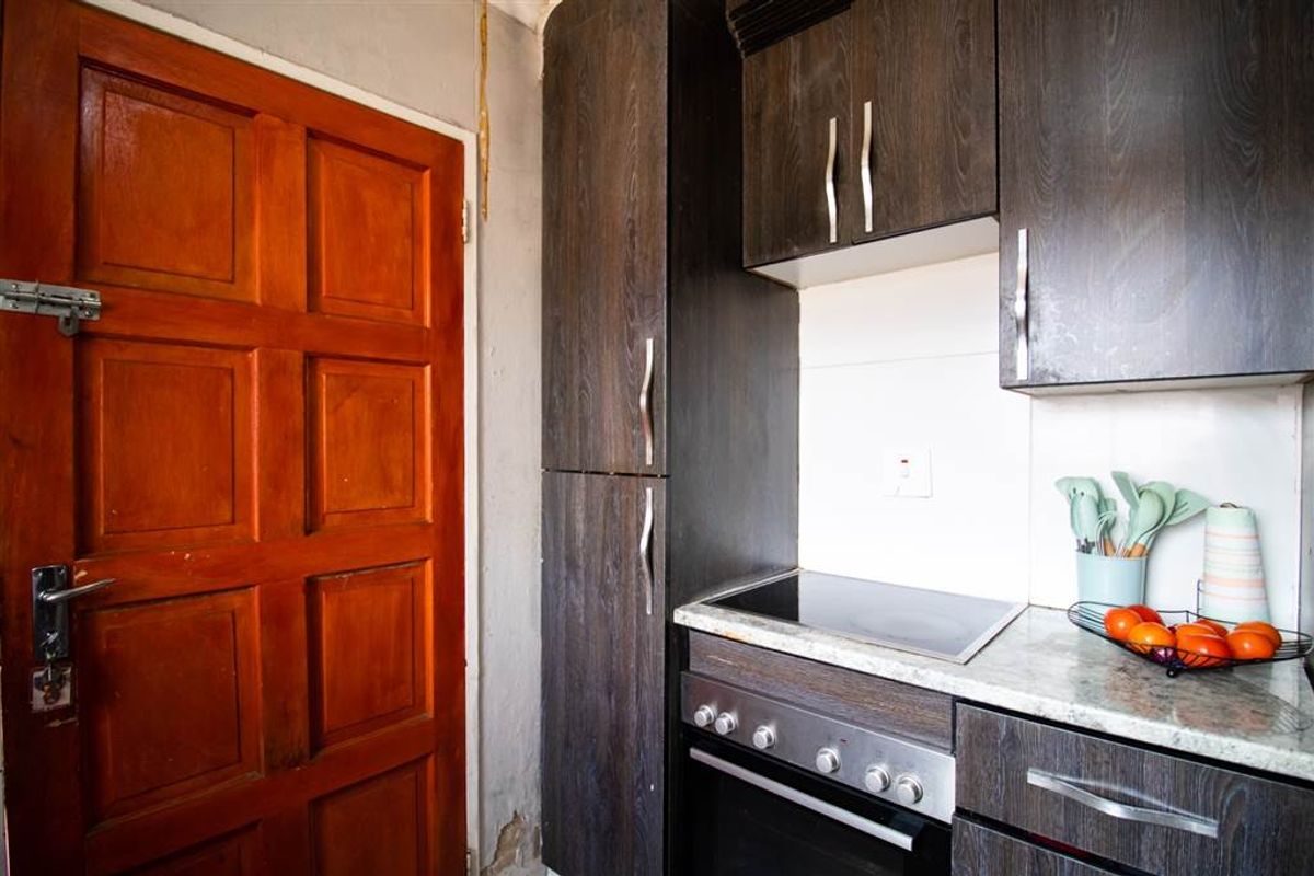 Compact kitchen area featuring dark wood-look cabinetry, integrated electric hob and oven, and stone-effect countertops, requiring some cosmetic wall repairs.