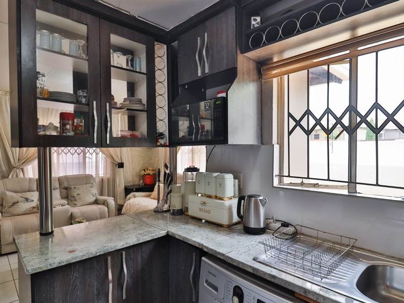 Compact kitchen featuring dark wood cabinetry, granite countertops, and a stainless steel sink, with security bars installed on the window.