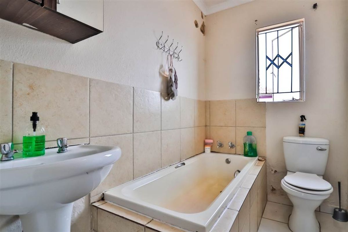 A dated bathroom featuring a pedestal basin, built-in bathtub, and toilet, requiring cosmetic updates and repairs to wall finishes and fixtures.