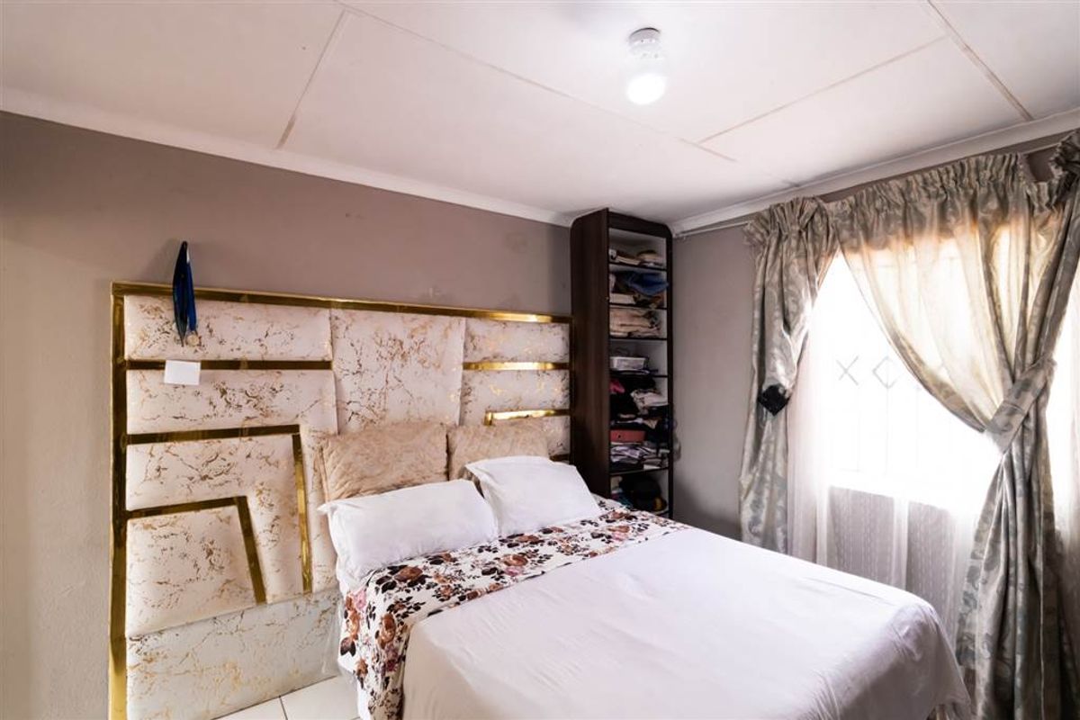 A bedroom featuring tiled flooring, a built-in shelving unit, and a decorative headboard. The ceiling shows visible signs of wear and cracking.