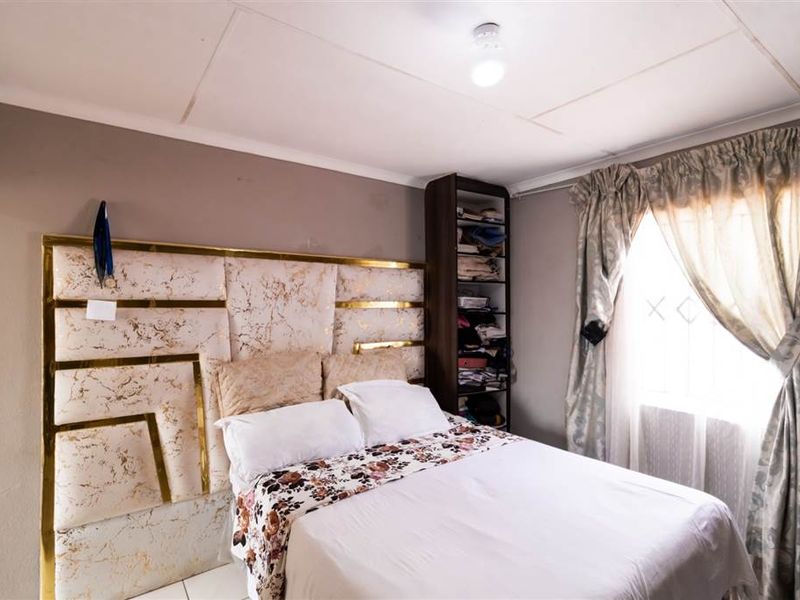 A bedroom featuring tiled flooring, a built-in shelving unit, and a decorative headboard. The ceiling shows visible signs of wear and cracking.