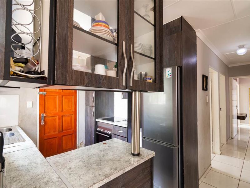 A functional kitchen featuring dark wood-look cabinetry, laminate countertops, and tiled flooring, with an adjacent hallway leading to other areas of the home.