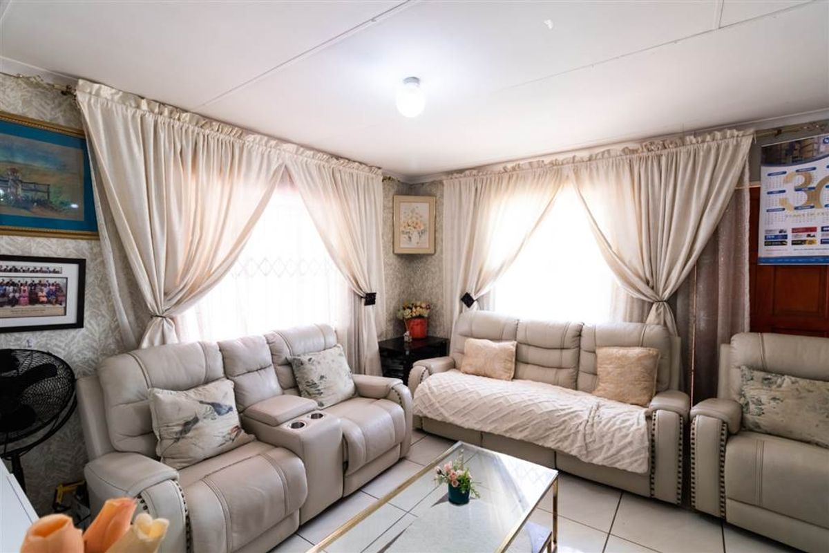 A comfortable living room featuring tiled flooring and natural light through large windows with curtains.