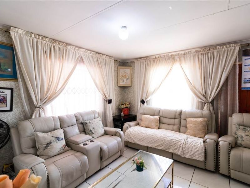 A comfortable living room featuring tiled flooring and natural light through large windows with curtains.