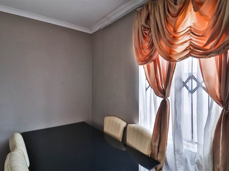A dining area featuring neutral wall finishes, coving, and a window fitted with security bars.