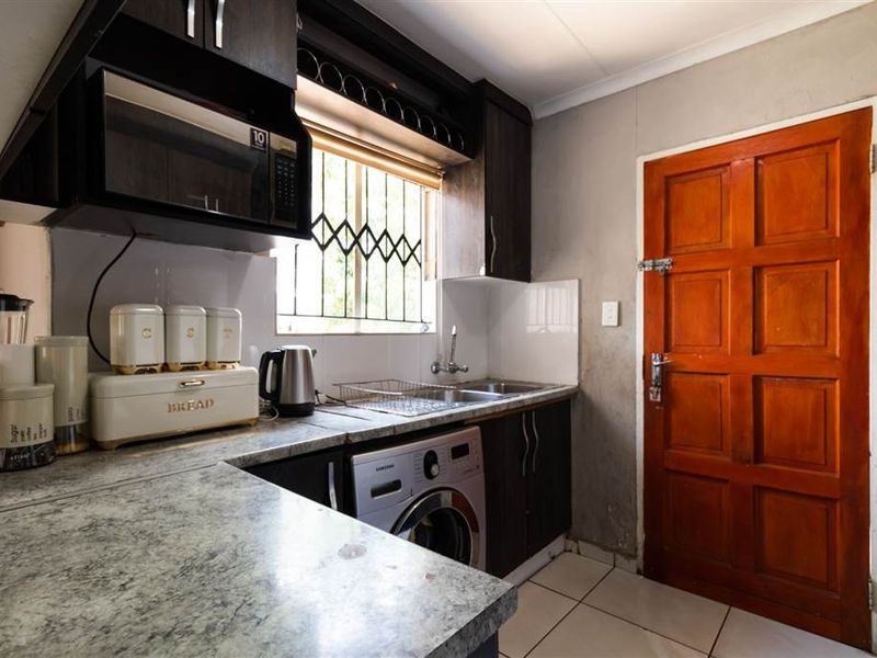 Compact kitchen featuring dark cabinetry, laminate countertops, built-in microwave, and tiled flooring with direct access to an exterior door.