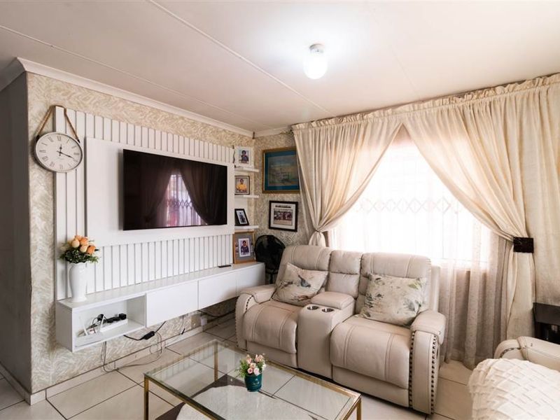A cozy living room featuring a built-in media unit, tiled flooring, and a window with security bars, offering a functional and well-maintained living space.