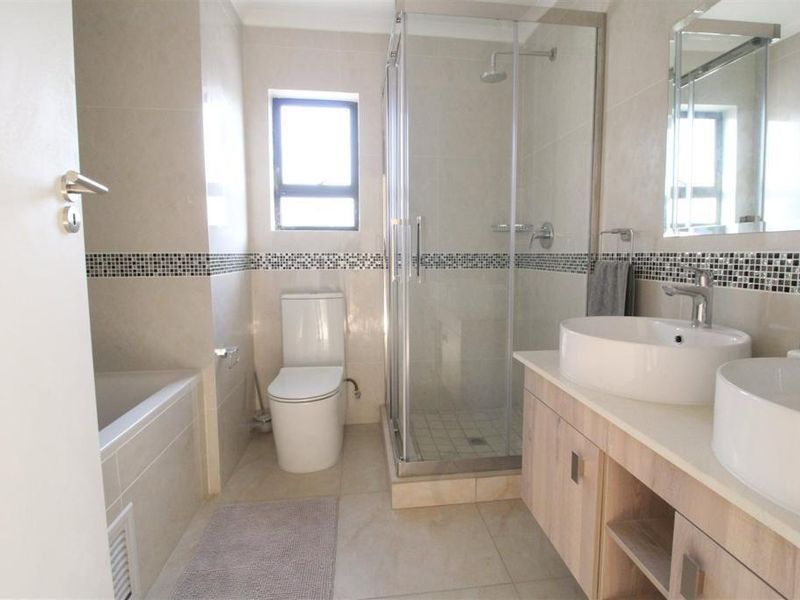 Modern bathroom featuring a double vanity with vessel sinks, a glass-enclosed shower, and a separate bathtub with neutral tiled finishes.