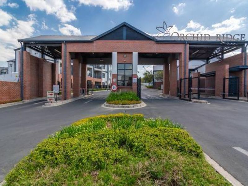 The main entrance and security gatehouse of the Orchid Ridge apartment complex, featuring brick construction and controlled access points.
