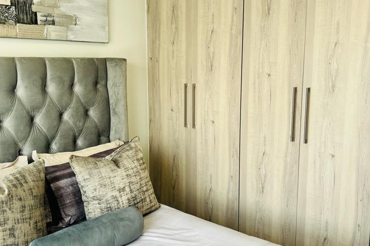 A well-maintained bedroom featuring light wood-grain built-in wardrobes and neutral wall finishes.