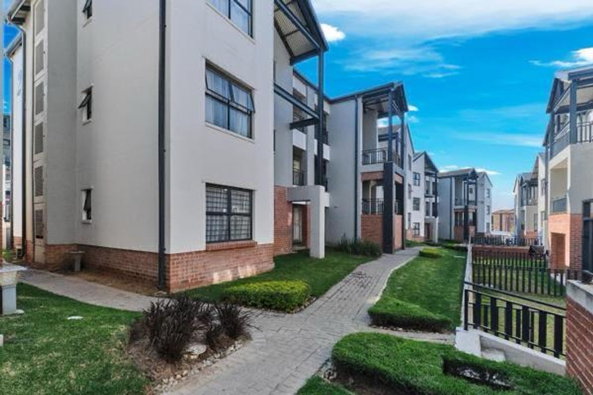 A view of the apartment complex exterior featuring paved walkways, landscaped garden areas, and modern brick and plaster building facades with balconies.