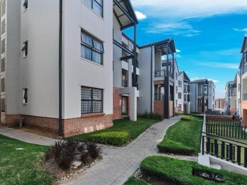 A view of the apartment complex exterior featuring paved walkways, landscaped garden areas, and modern brick and plaster building facades with balconies.