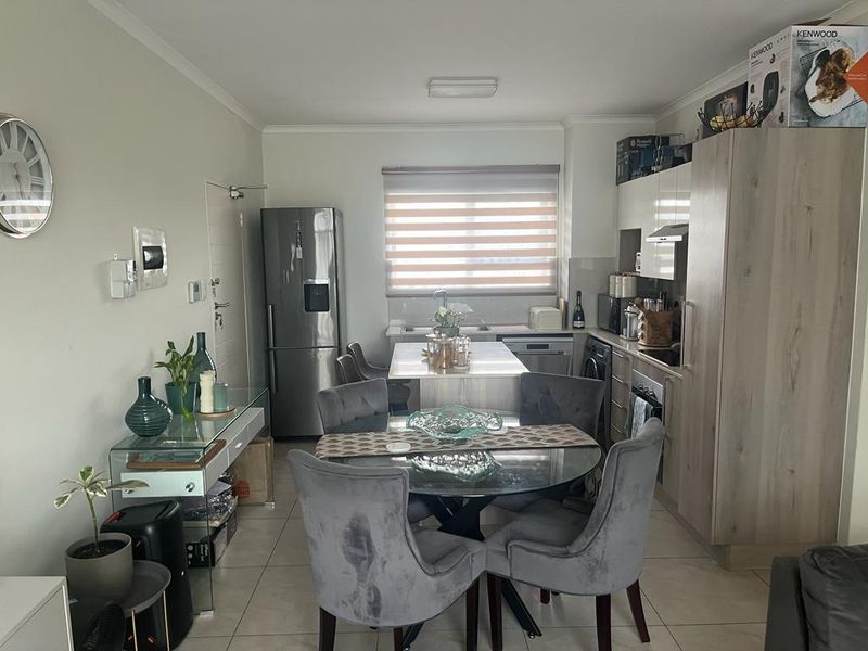 Modern open-plan kitchen and dining area featuring contemporary cabinetry, a central island, integrated appliances, and neutral tiled flooring.