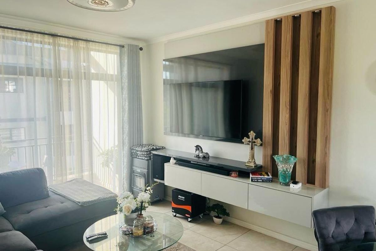 A modern living room featuring a sleek wall-mounted media console, decorative timber slat wall paneling, and large windows with sheer curtains.