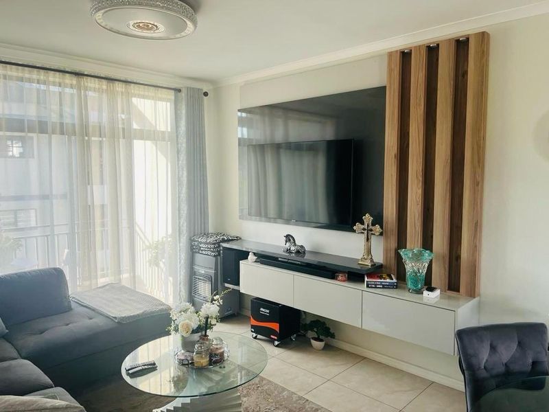 A modern living room featuring a sleek wall-mounted media console, decorative timber slat wall paneling, and large windows with sheer curtains.