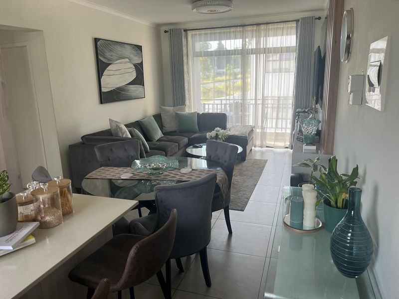 A well-maintained open-plan living and dining area featuring tiled floors, neutral walls, and a sliding glass door leading to a balcony.
