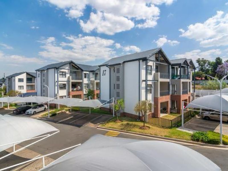 Exterior view of a modern apartment complex featuring multiple residential blocks, paved parking areas with shade cloth carports, and private balconies.