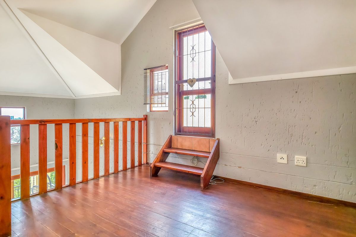 An empty loft-style bedroom featuring wooden flooring, a vaulted ceiling, and a wooden balustrade overlooking the lower level.