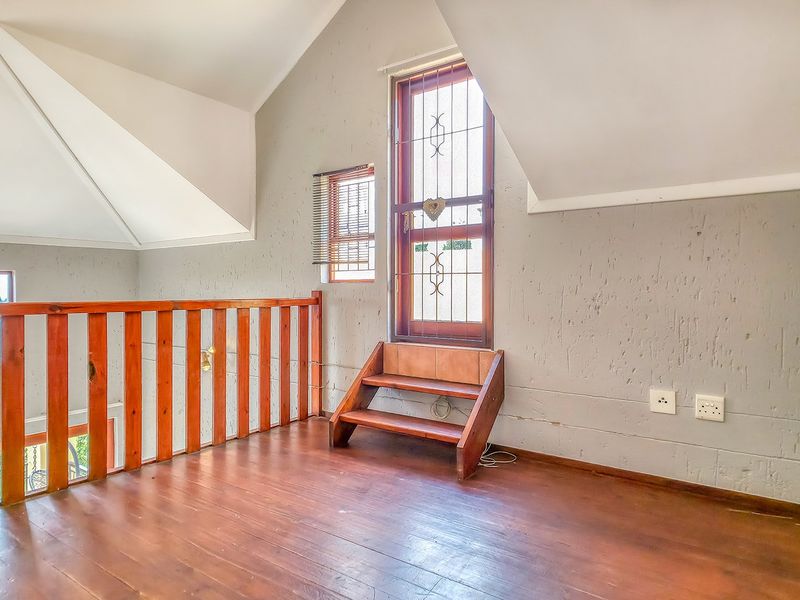 An empty loft-style bedroom featuring wooden flooring, a vaulted ceiling, and a wooden balustrade overlooking the lower level.