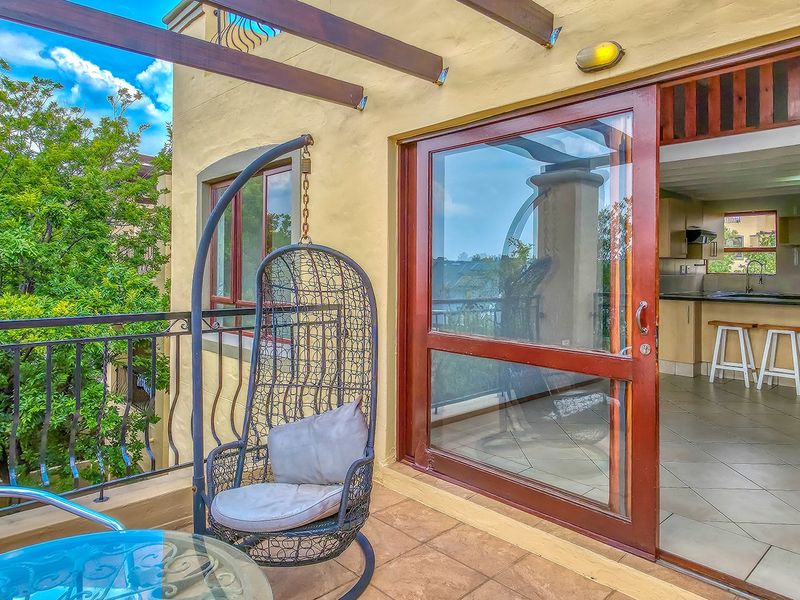 A covered balcony featuring tiled flooring, a wrought iron railing, and a timber pergola, providing seamless indoor-outdoor flow to the adjacent open-plan living area.