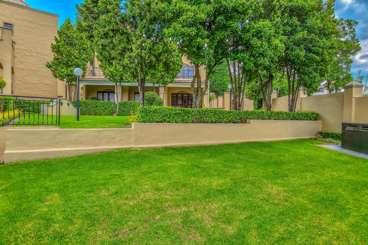 A well-maintained rear garden featuring a manicured lawn, established trees, neat hedging, and a solid perimeter wall with wrought iron accents.