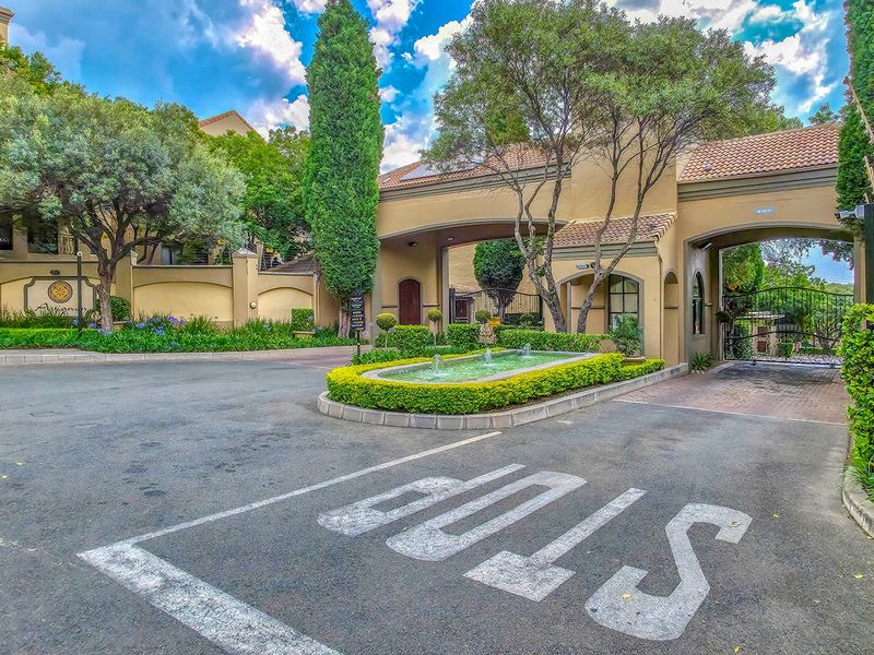 The secure entrance to the apartment complex features a gated access point, a decorative fountain, and well-maintained landscaped gardens.