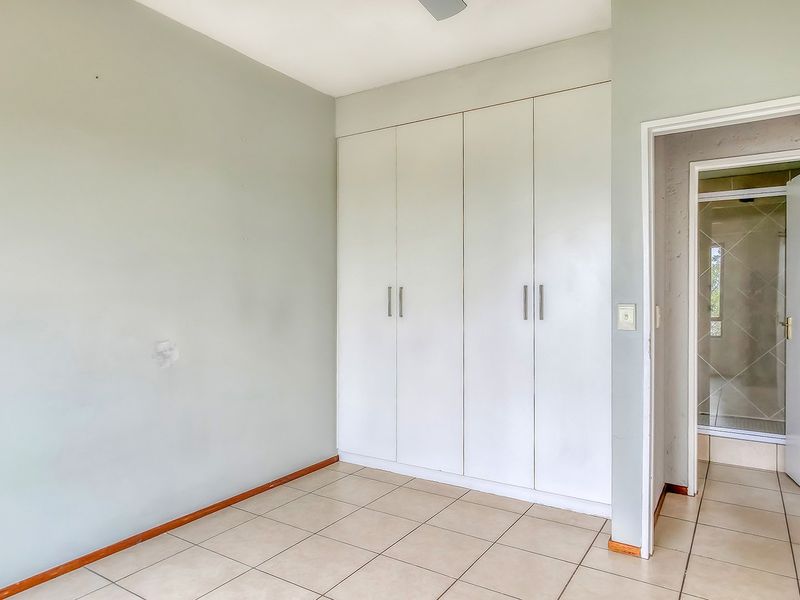 A vacant bedroom featuring neutral tiled flooring, built-in cupboards, and an adjoining en-suite bathroom.