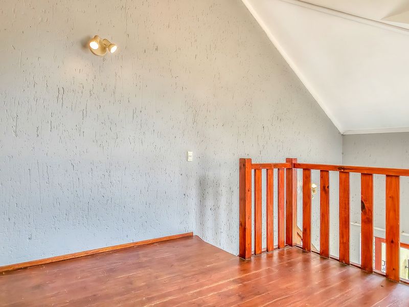 An empty loft-style living area featuring wooden flooring, a vaulted ceiling, and a wooden balustrade overlooking the lower level.