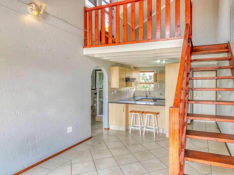 Open plan living area featuring a wooden staircase leading to a mezzanine level, adjacent to a functional kitchen with built-in cabinetry.