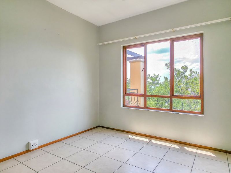 A bright, empty bedroom featuring neutral wall paint, tiled flooring, and a large timber-framed window providing natural light.