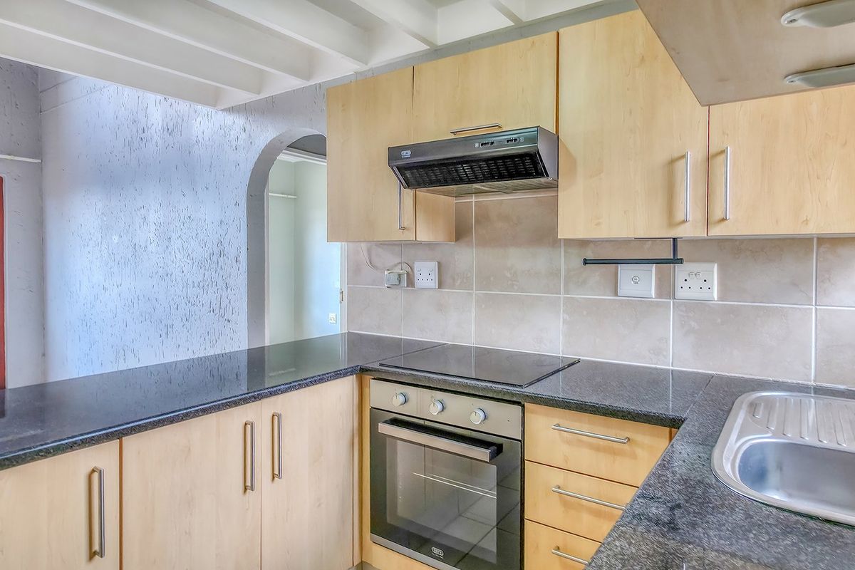 Functional kitchen featuring light wood cabinetry, granite countertops, built-in oven, electric hob, and a stainless steel sink with a tiled backsplash.