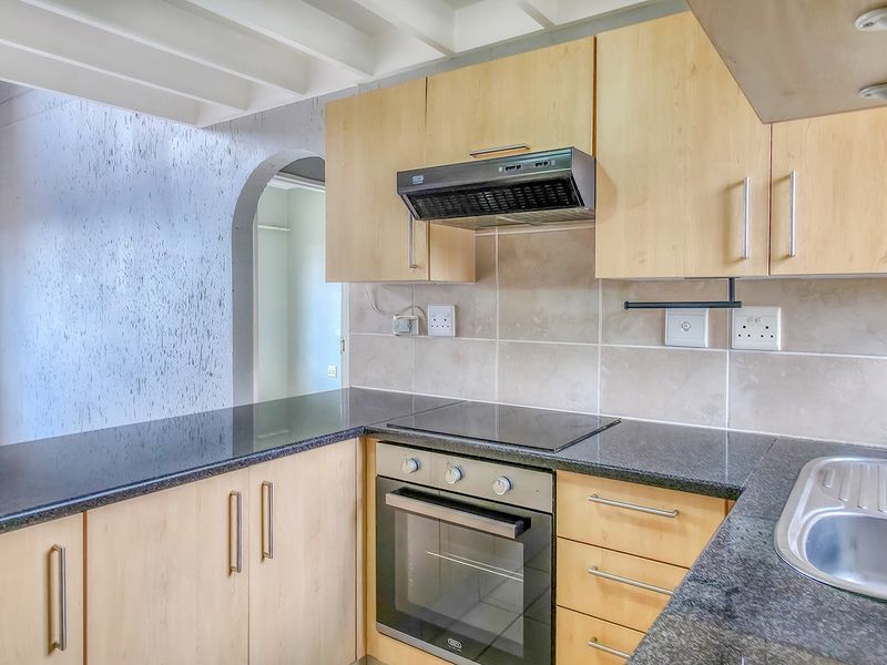 Functional kitchen featuring light wood cabinetry, granite countertops, built-in oven, electric hob, and a stainless steel sink with a tiled backsplash.