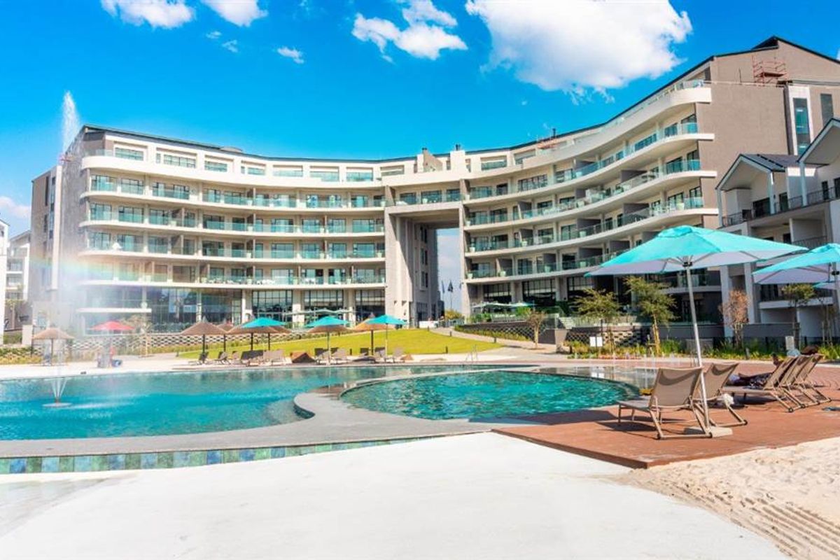 A modern apartment complex featuring a large swimming pool, water fountain, landscaped grounds, and private balconies for residents.