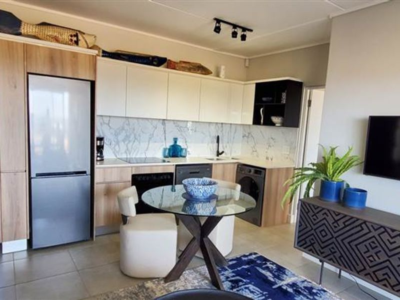 Modern open-plan living area featuring a compact kitchen with marble-look backsplash, integrated appliances, and tiled flooring, seamlessly flowing into the lounge space.
