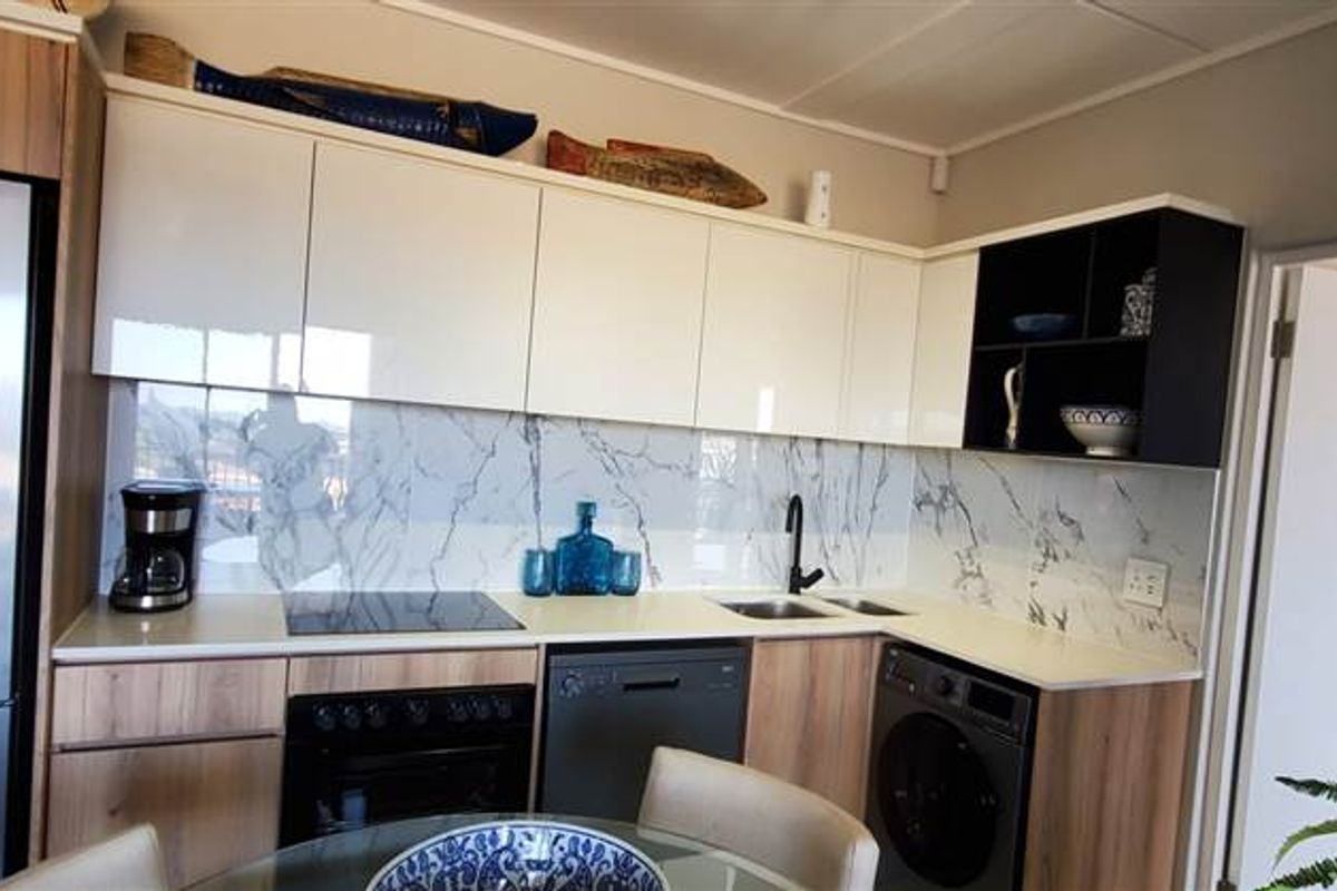 Modern kitchen featuring sleek white and wood-tone cabinetry, marble-look splashback, and integrated appliances including an oven, hob, dishwasher, and washing machine.