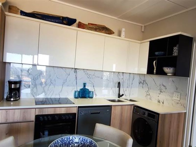 Modern kitchen featuring sleek white and wood-tone cabinetry, marble-look splashback, and integrated appliances including an oven, hob, dishwasher, and washing machine.