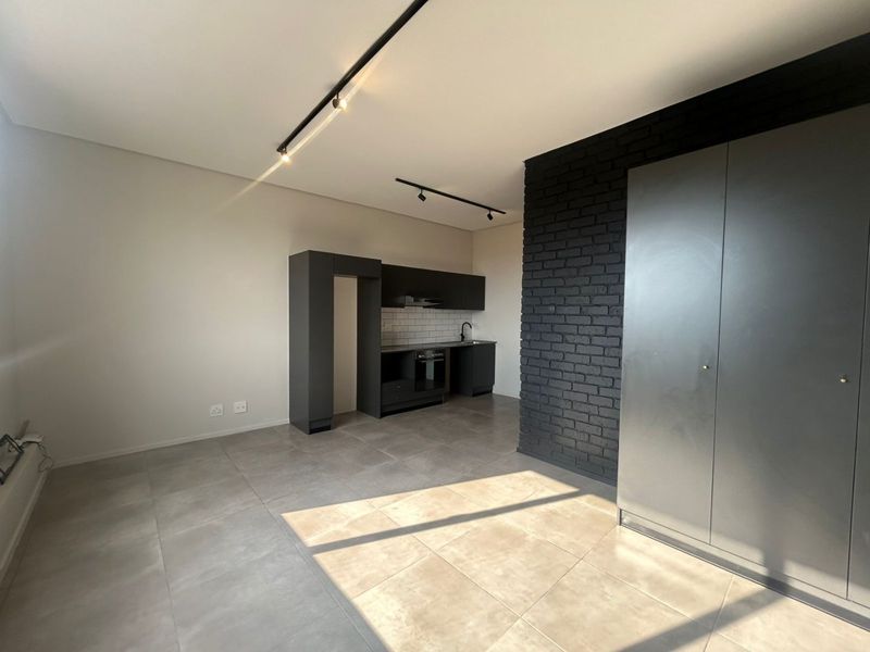 Modern open-plan living area featuring a sleek kitchen with built-in appliances, tiled floors, and a striking black exposed brick feature wall.