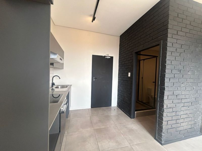 Modern open-plan apartment featuring a sleek kitchen with built-in cabinetry, electric hob, and a striking black exposed brick feature wall leading to the bathroom.