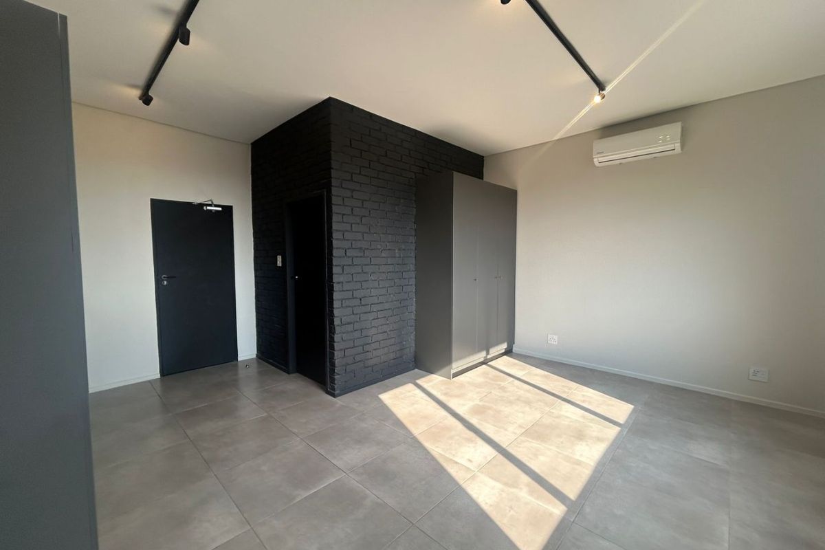 A modern, minimalist bedroom featuring a striking black brick accent wall, neutral tiled flooring, built-in wardrobe, and efficient split-system air conditioning.