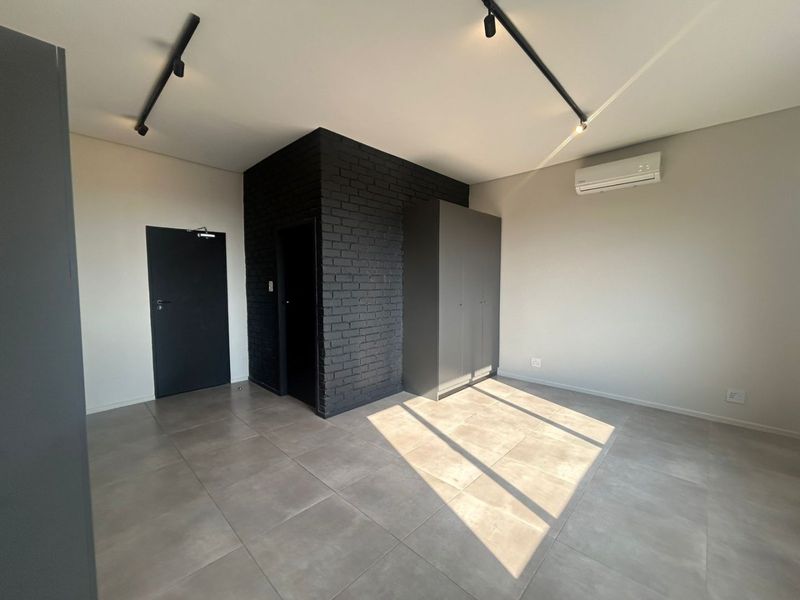 A modern, minimalist bedroom featuring a striking black brick accent wall, neutral tiled flooring, built-in wardrobe, and efficient split-system air conditioning.