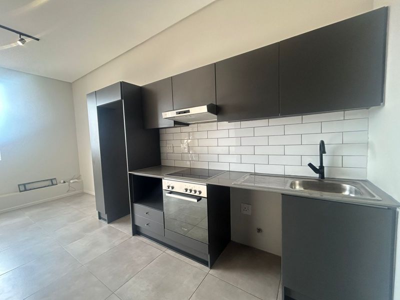 Modern kitchen featuring dark cabinetry, subway tile backsplash, integrated oven and hob, and stainless steel sink with contemporary matte black tap.