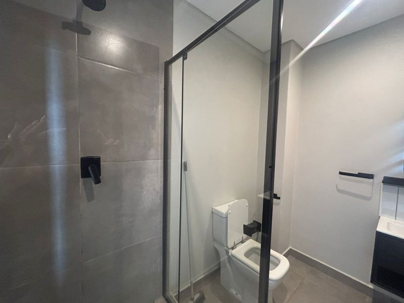 Modern bathroom featuring a glass-enclosed shower, contemporary toilet, and vanity with clean tiled finishes and matte black fixtures.