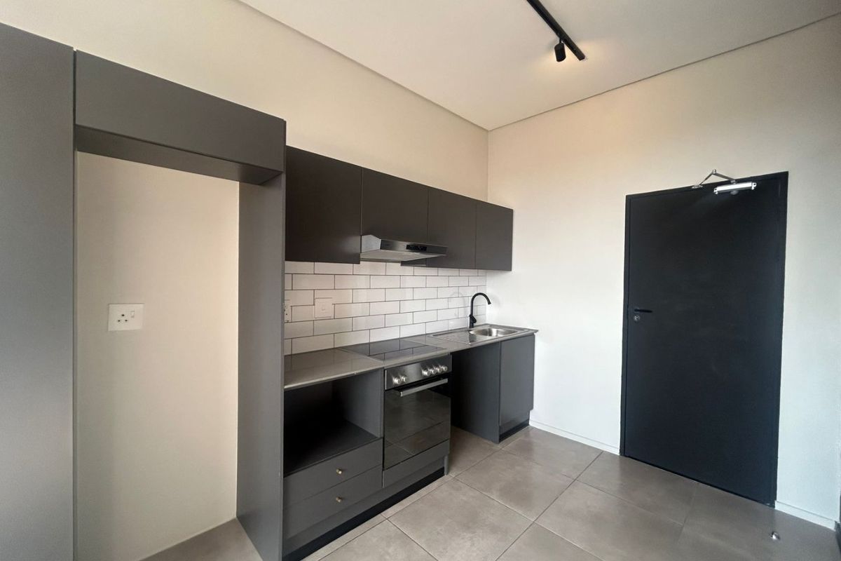 Modern kitchen featuring dark grey cabinetry, subway tile backsplash, integrated oven and hob, and sleek black fixtures in a clean, minimalist space.