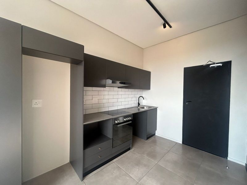 Modern kitchen featuring dark grey cabinetry, subway tile backsplash, integrated oven and hob, and sleek black fixtures in a clean, minimalist space.